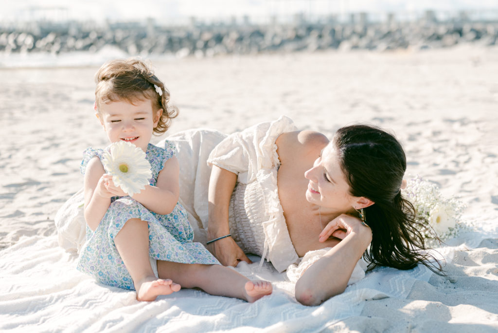 Mom and daughter smelling a daisy flower on the beach