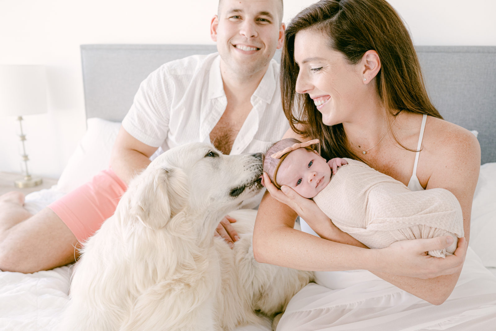 Dog licking baby's head on the bed while the family is smiling in Fort Lauderdale