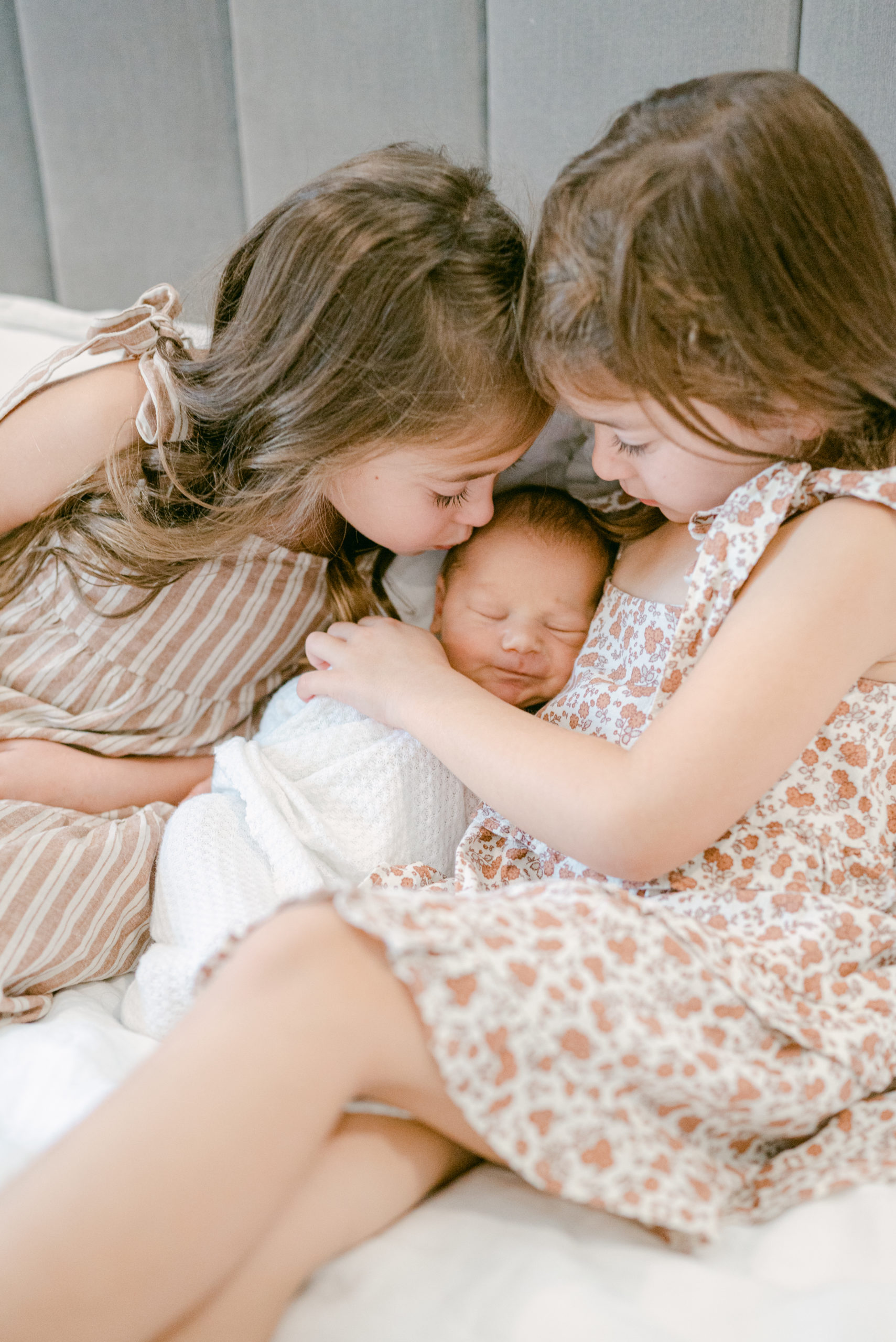 Twin girls kissing their newborn baby brother