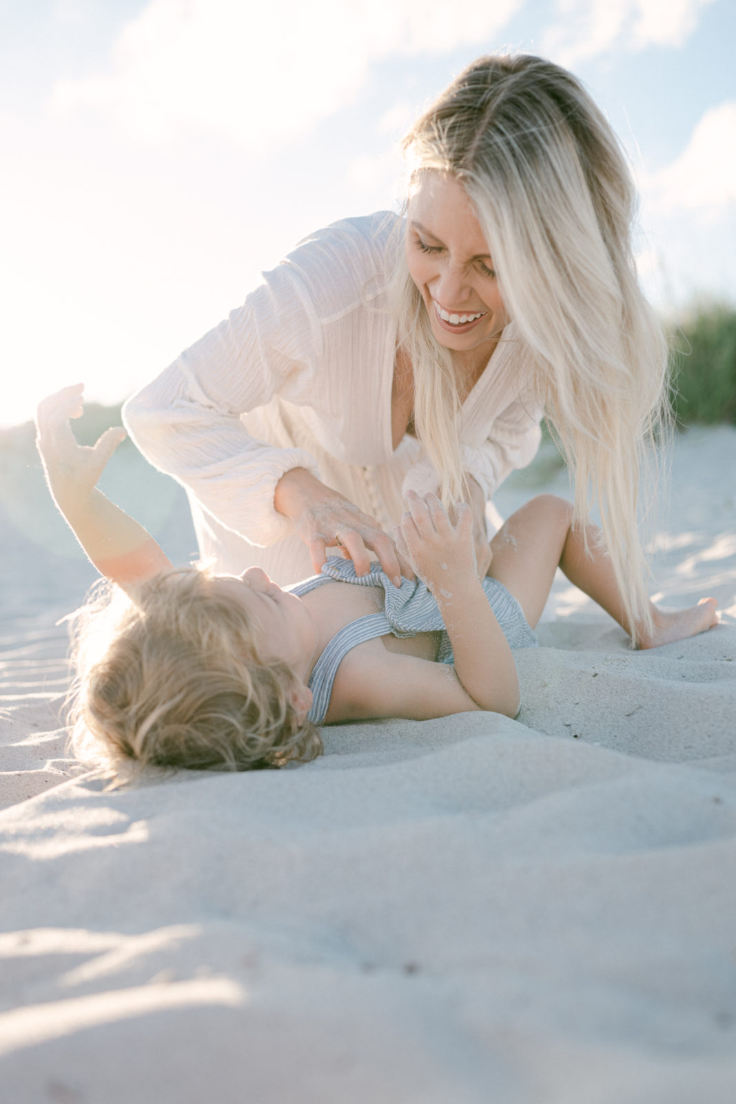 Mom tickling her son on the sand, both are having fun