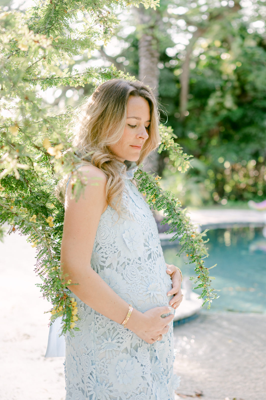 Mom to be looking down at her bump next to a swimming pool 