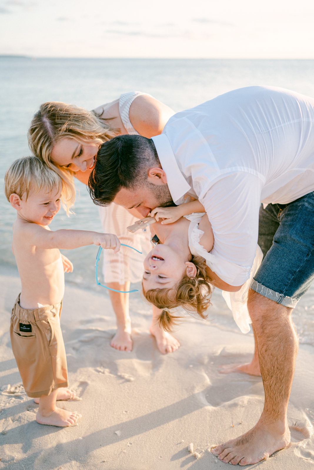 Dad is tickling his daughter upside down on the beach, family having fun