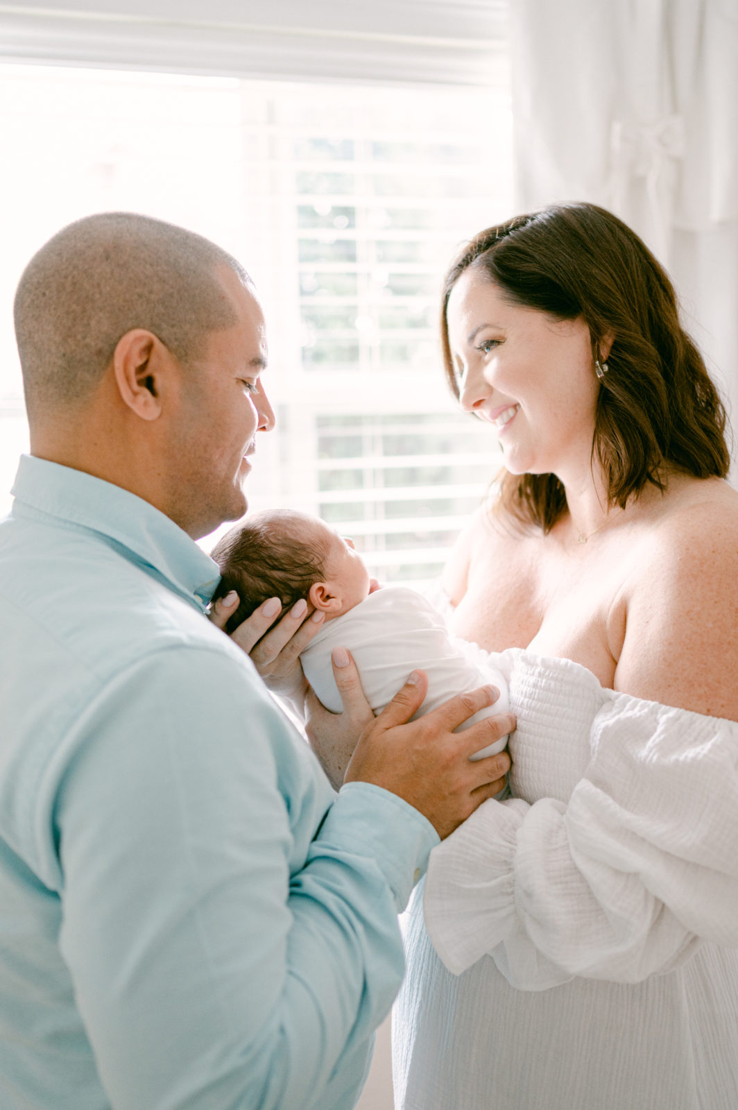 Lifestyle Newborn Photos of dad and mom holding baby and smiling at each other