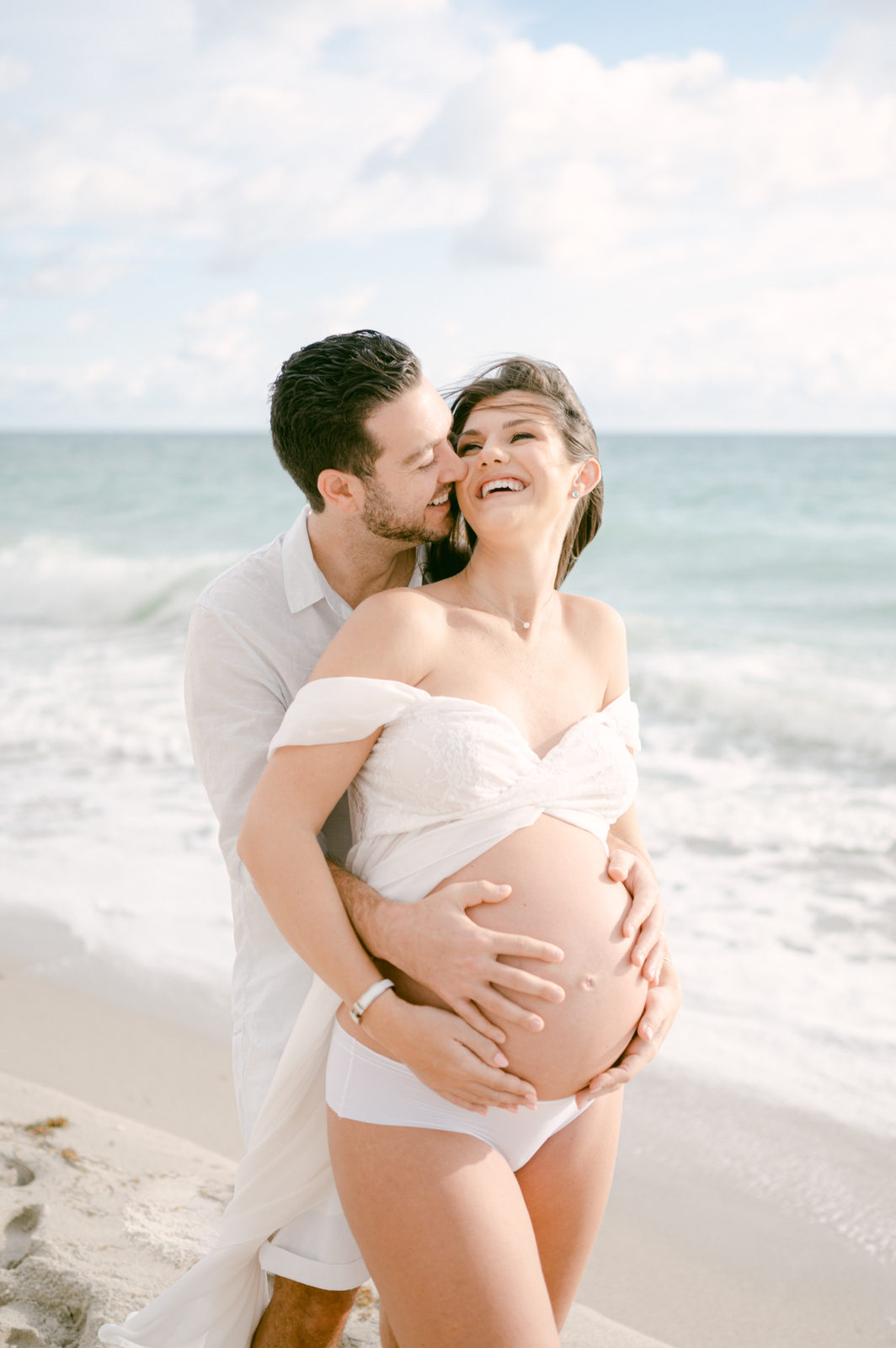 Laughing pregnant couple taking maternity photos on the beach