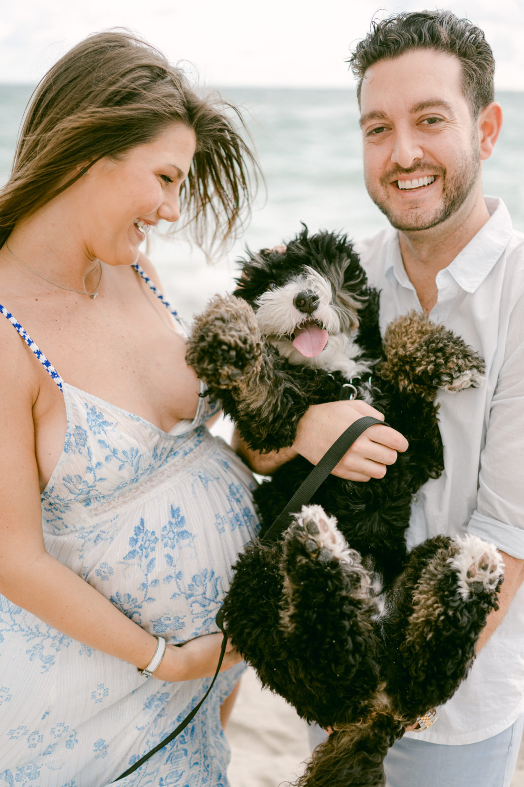 Pregnant couple taking pictures with their family dog on the beach