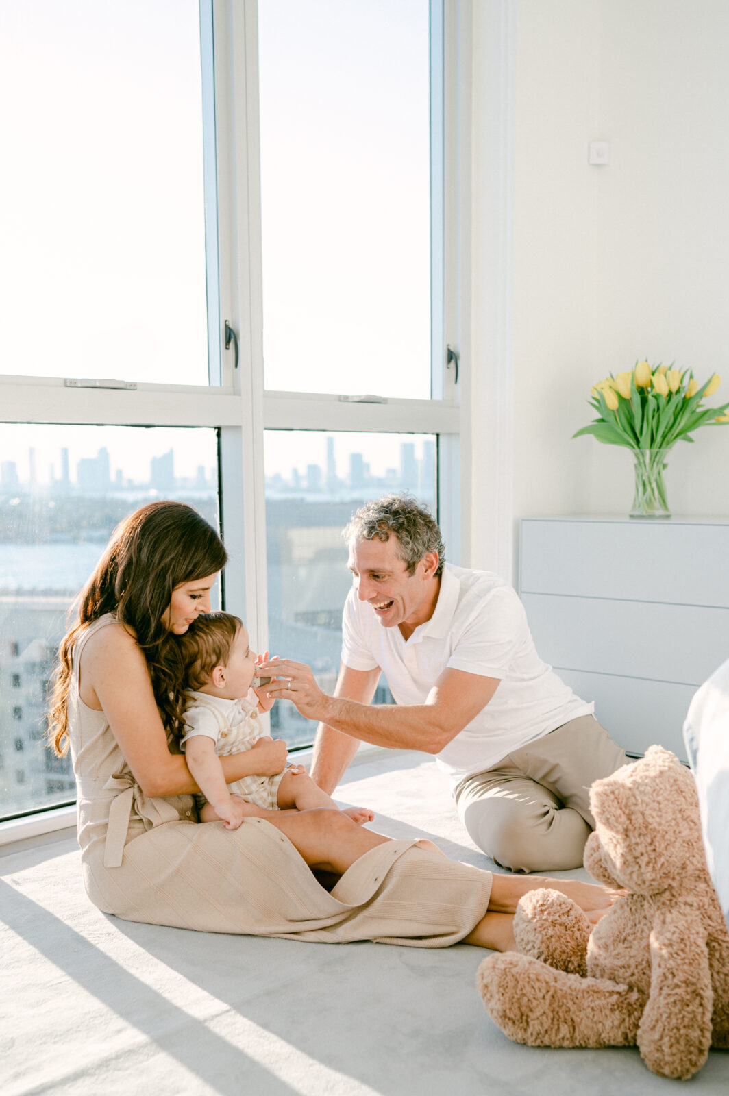Family with toddler playing in sunny bedroom with Miami skyline in the background