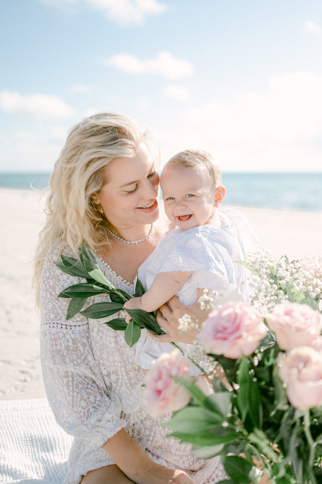Mom snuggling with her baby girl on the beach with flowers