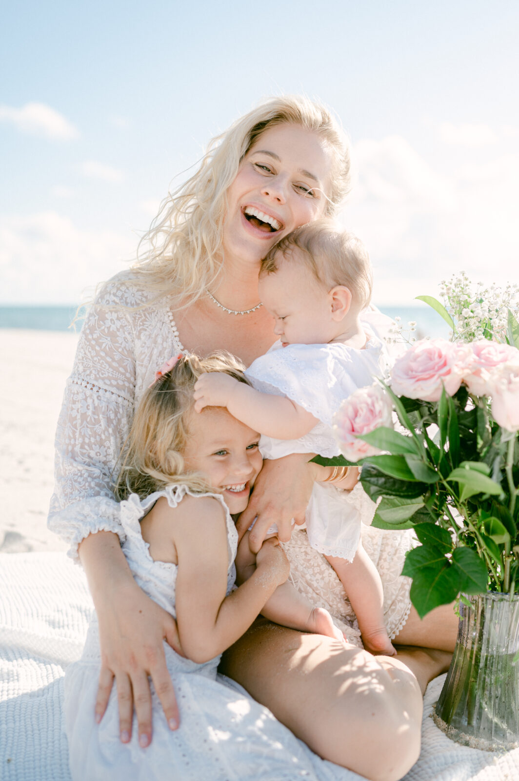 Mom laughing with her 2 kids on the beach with flowers 