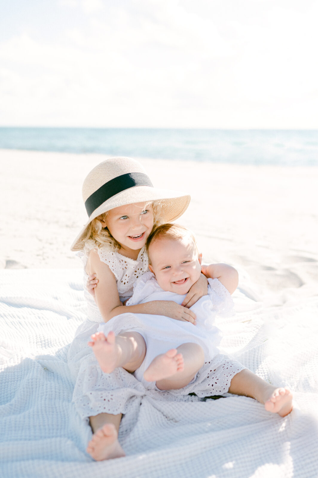 Siblings with sun hat snuggling on the beach by Miami photographer