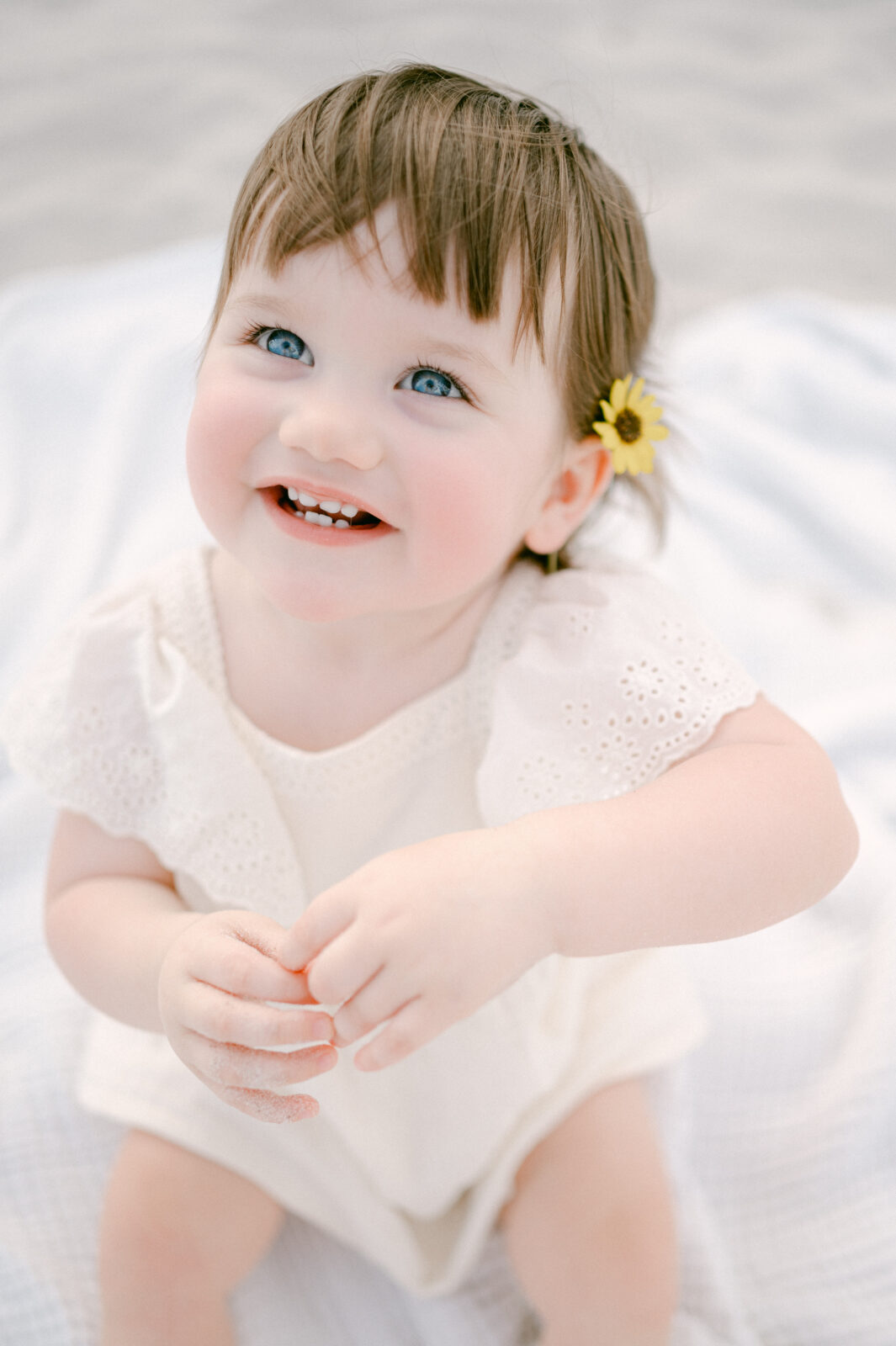 Blue eyed little girl smiling with a yellow flower on her ear