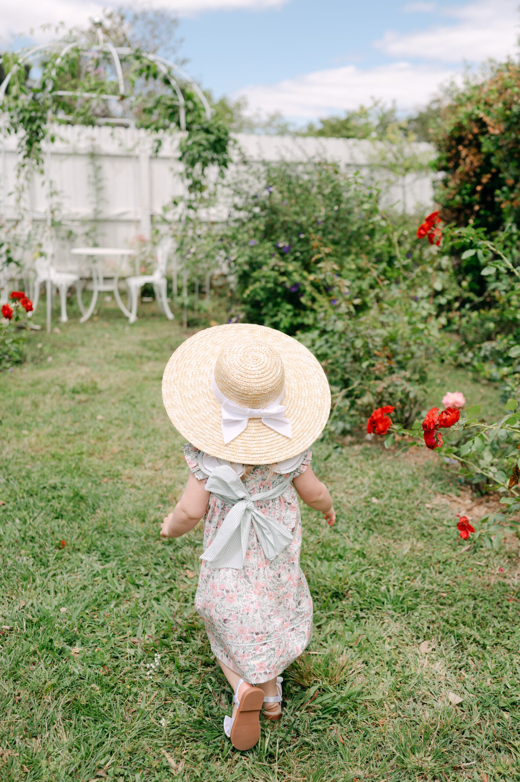Little girl with summer hat running in a garden with roses